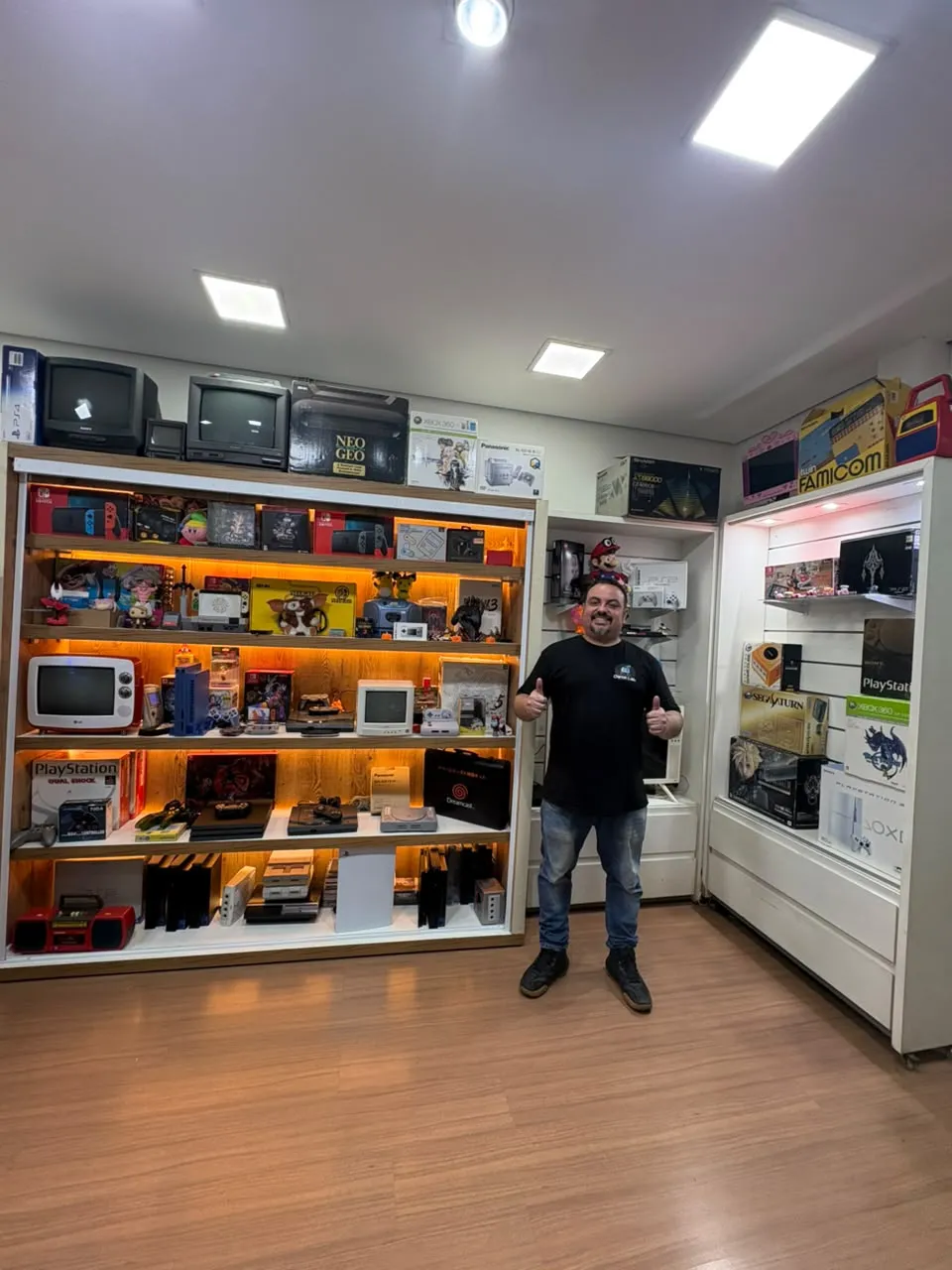 Renato ao lado das estantes de consoles da Game Lab