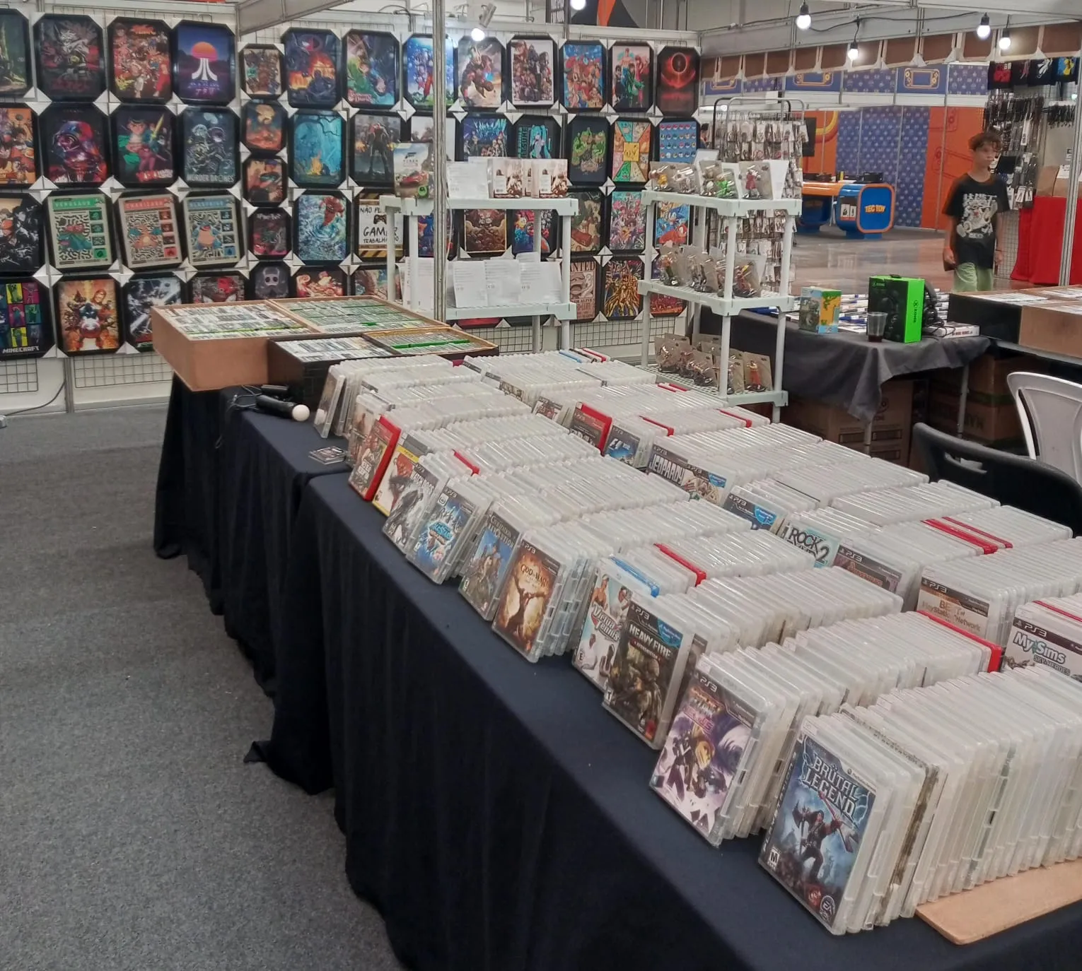 Mesa de jogos com quadros de personagens ao fundo no estande da House of Games
