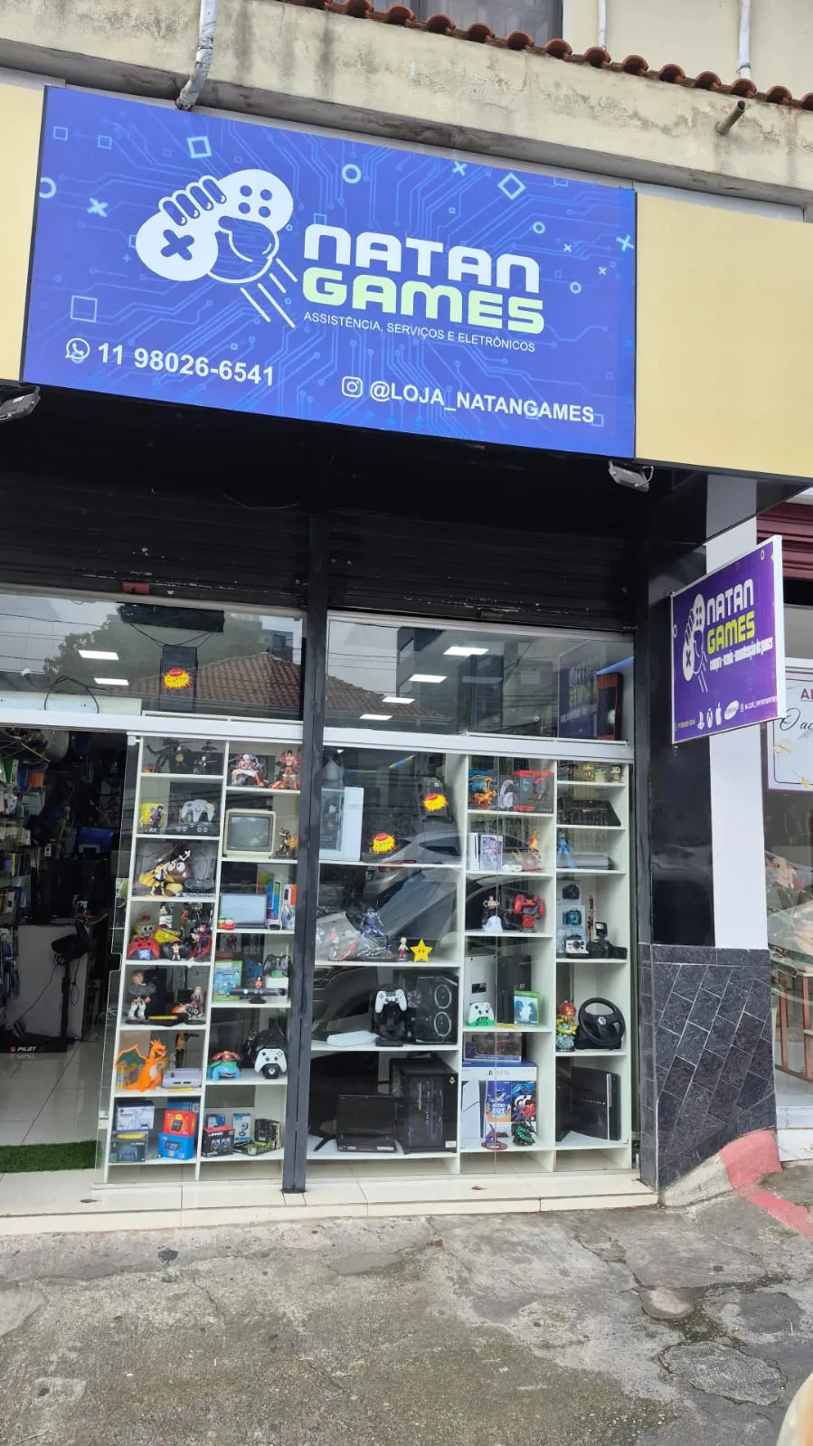 Fachada da Natan Games, em Mauá, com letreiro azul e vitrine de consoles e colecionáveis