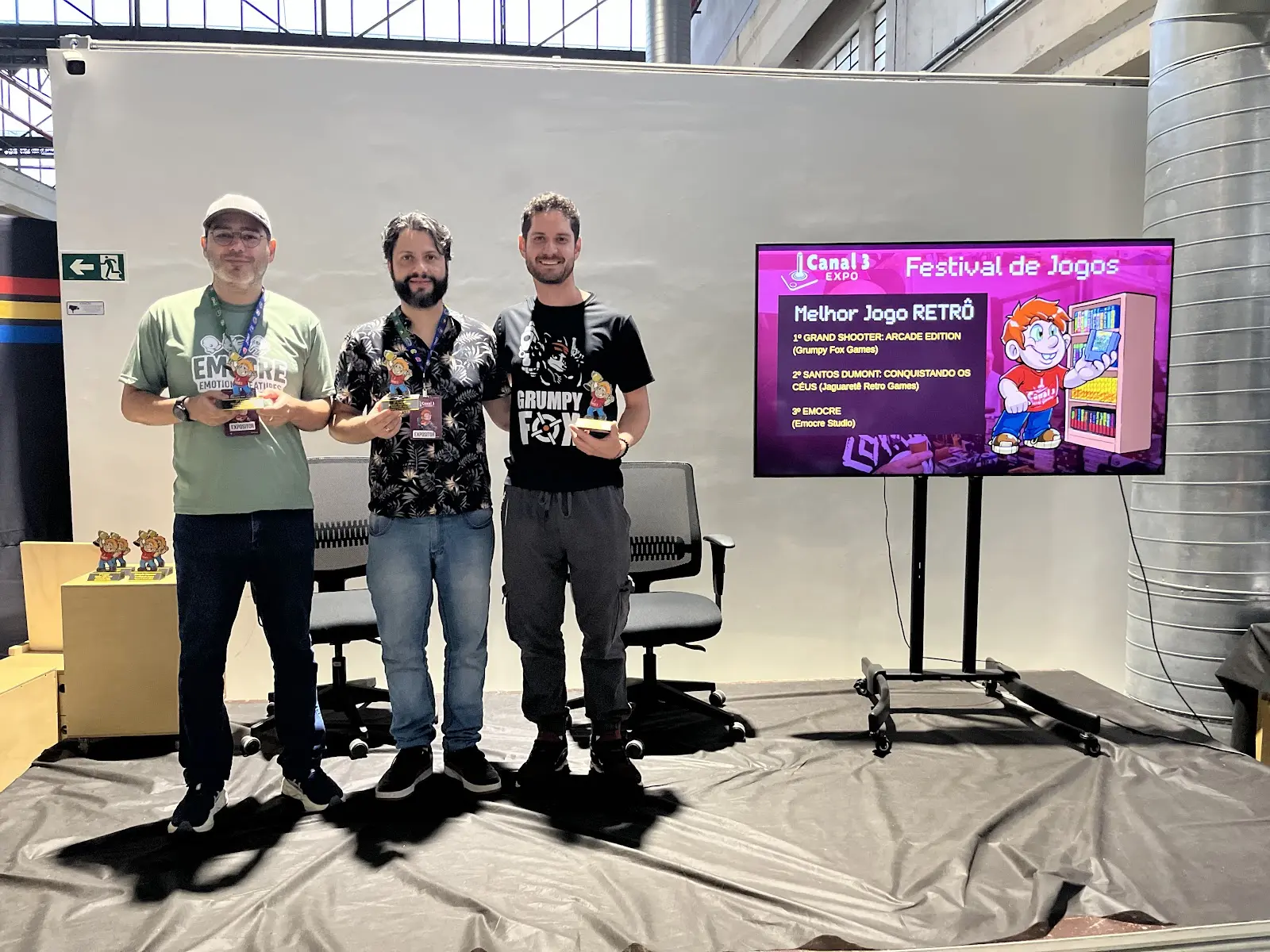 Vencedores do Melhor Jogo RETRO de 2025 no palco com troféus e o telão do Festival de Jogos